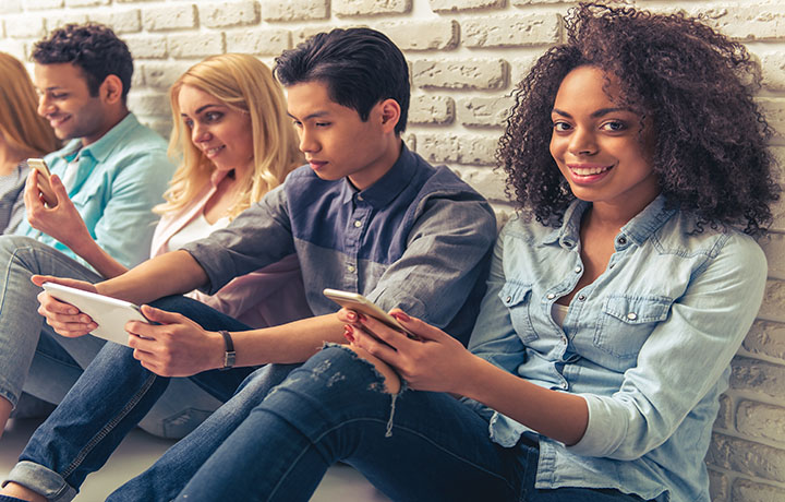 Students sitting against a wall looking at their phones