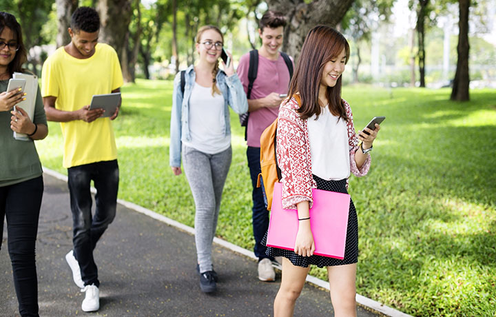 Students walking along a path with eyes on their phones